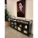 Featuring Shadow Box Sideboard - Black by Four Hands at Amethyst Home. This Shadow Box Sideboard gives your inner collector a place to play. Store prized possessions behind clear glass fronts, with black-finished metal casing and brass hardware for contrast.
Overall Dimensions: 70"W x 17.25"L x 35"H
Colors: Black, Weathered Bronze, Clear Glass, Tempered .  Amethyst Home provides interior design, new home construction design consulting, vintage area rugs, and lighting in the Kansas City metro area.