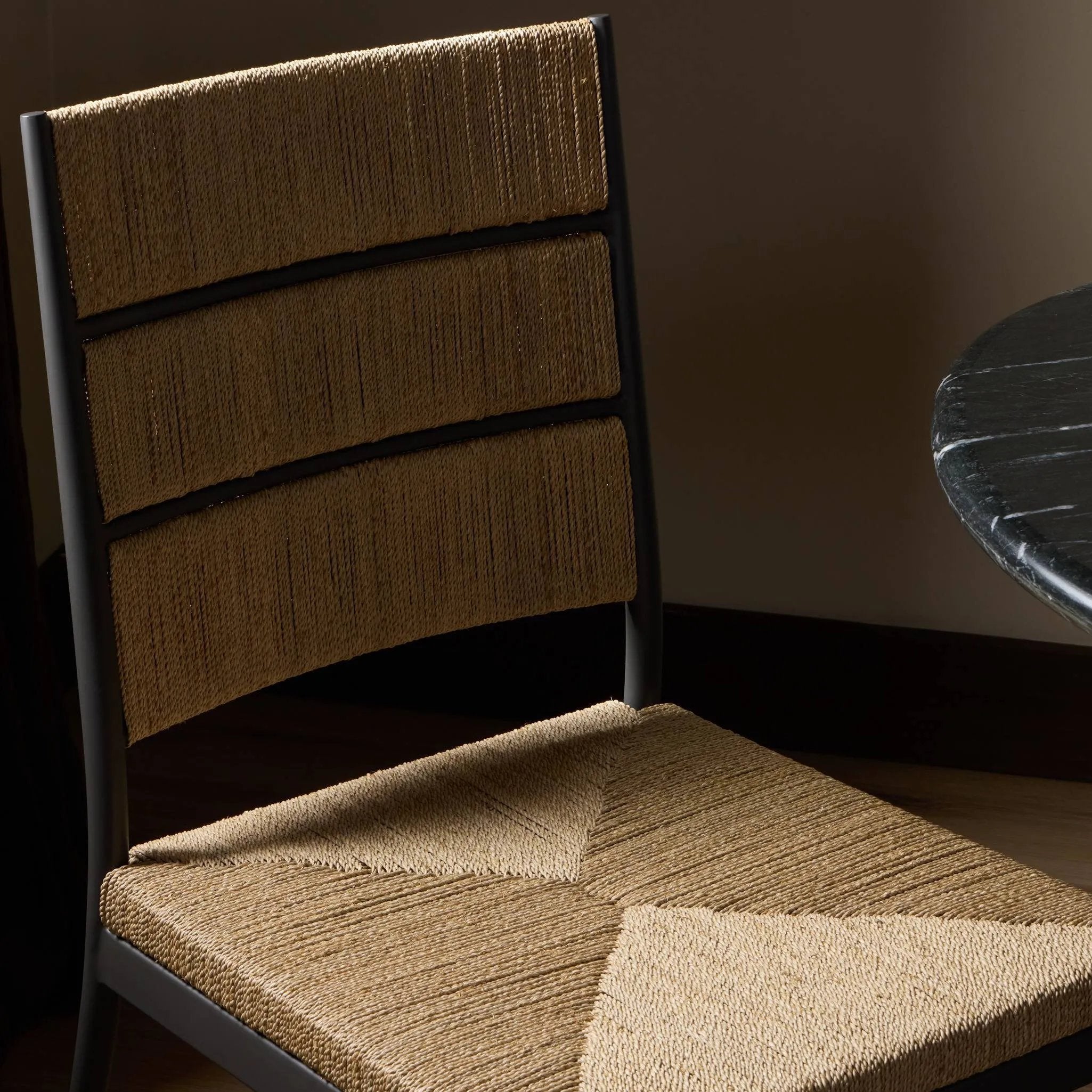 A steel dining chair frame is softened and paired with natural woven fibers. Thin, tapered legs and a tall channeled back cre