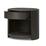 Rich contours bring character to the bedside. A round black-finished oak table has a spacious cubby and a single drawer with metal glides and a bronzed pull Amethyst Home provides interior design, new home construction design consulting, vintage area rugs, and lighting in the San Diego metro area.