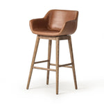 A midcentury-inspired counter stool gets refreshed with a modern memory swivel and chestnut top-grain leather. Slim, tapered oak legs balance a curved seat Amethyst Home provides interior design, new home construction design consulting, vintage area rugs, and lighting in the Park City metro area.