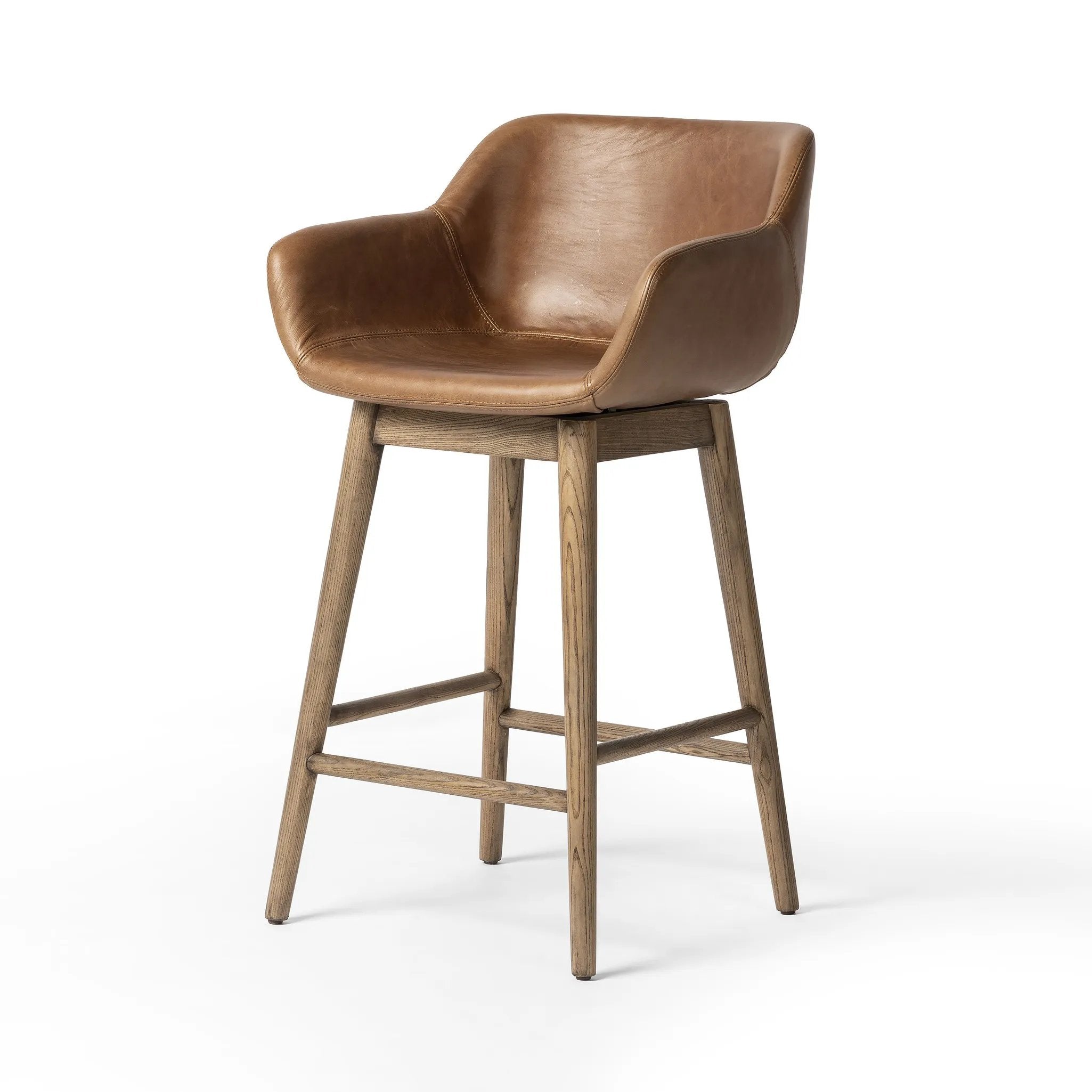 A midcentury-inspired counter stool gets refreshed with a modern memory swivel and chestnut top-grain leather. Slim, tapered oak legs balance a curved seat Amethyst Home provides interior design, new home construction design consulting, vintage area rugs, and lighting in the Seattle metro area.