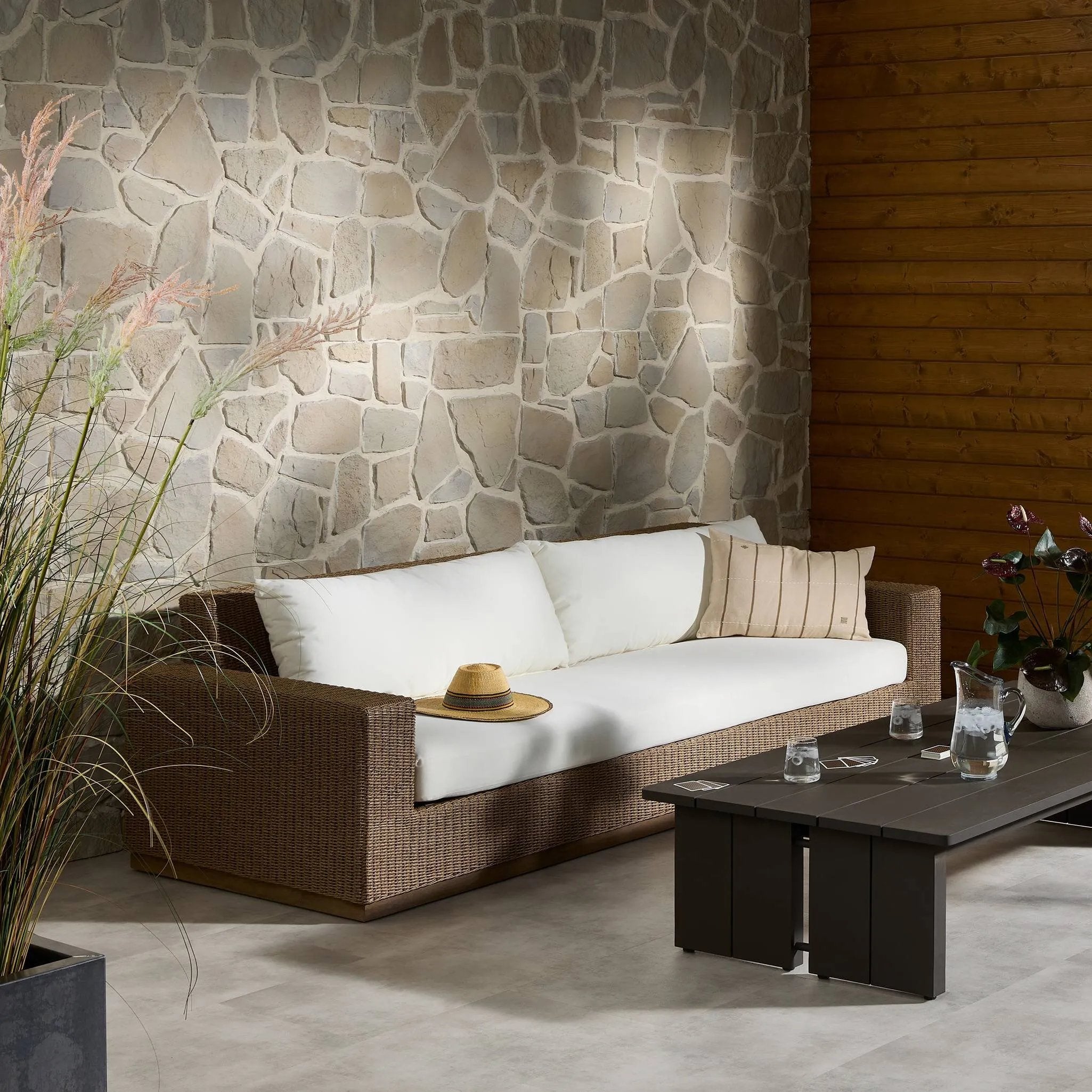 Elevate your outdoors. A wide-format outdoor sofa features a faux hyacinth frame and plinth base. Linear details and a boxy silhouette make this piece truly timeless, while knife-edge back cushions soften the whole look. Upholstered in 100% olefin, known for its UV-resistant, water-repellent and quick-drying abilities. Amethyst Home provides interior design, new home construction design consulting, vintage area rugs, and lighting in the Washington metro area.
