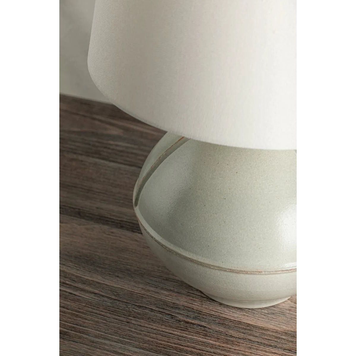 Inspired by rustic pottery, this table lamp's beautifully shaped base is crafted of pale sage ceramic giving it an earthy pale green tone. The off white linen shade pairs naturally and casts a soft glow. Raised seamlines and a reactive glaze that allows hints of the natural ceramic to peek through, give the fixture a hand-thrown, crafted feel. Amethyst Home provides interior design, new home construction design consulting, vintage area rugs, and lighting in the Laguna Beach metro area.