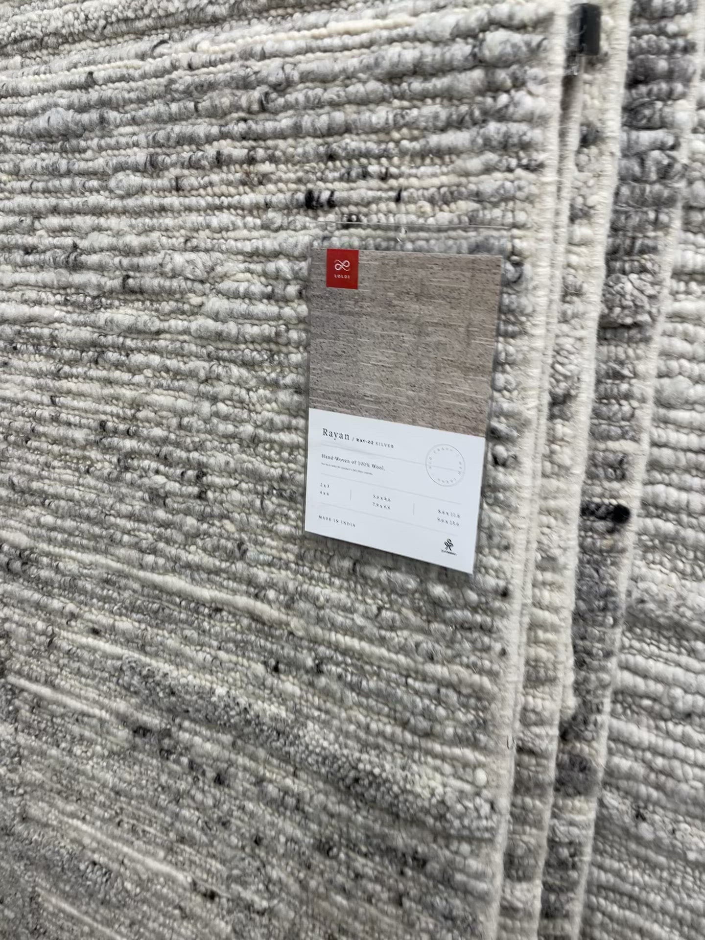 Load video: Hand-woven of 100% wool in India, the Rayan Silver Area Rug sets the tone for a calming atmosphere. Each design is crafted of textural highs and lows paired with neutral tones to create and engaging understatement. The perfect rug for your bedroom, office, or other medium traffic area.   Hand Woven 93% Wool | 5% Cotton | 2% Other Fibers Pile RAY-02 Silver