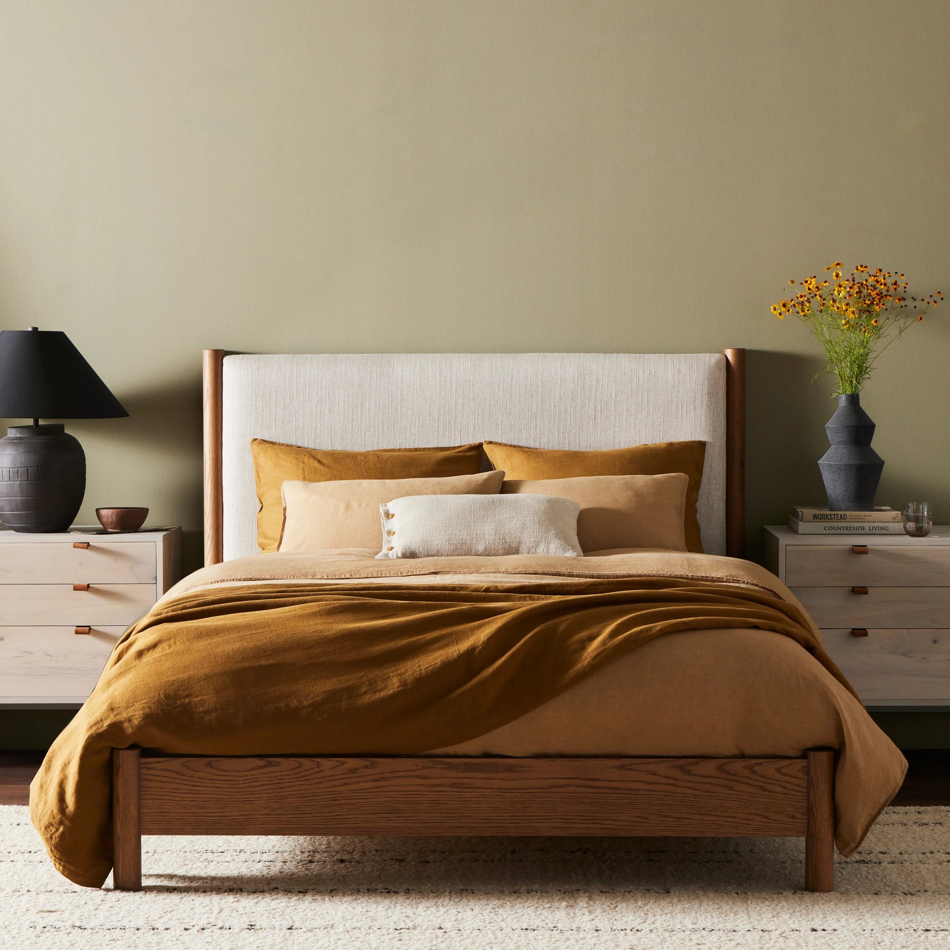 Rounded, chunky dowel legs in an amber oak finish frame the neutral, linen-like upholstered headboard of this bed frame Amethyst Home provides interior design, new home construction design consulting, vintage area rugs, and lighting in the Omaha metro area.